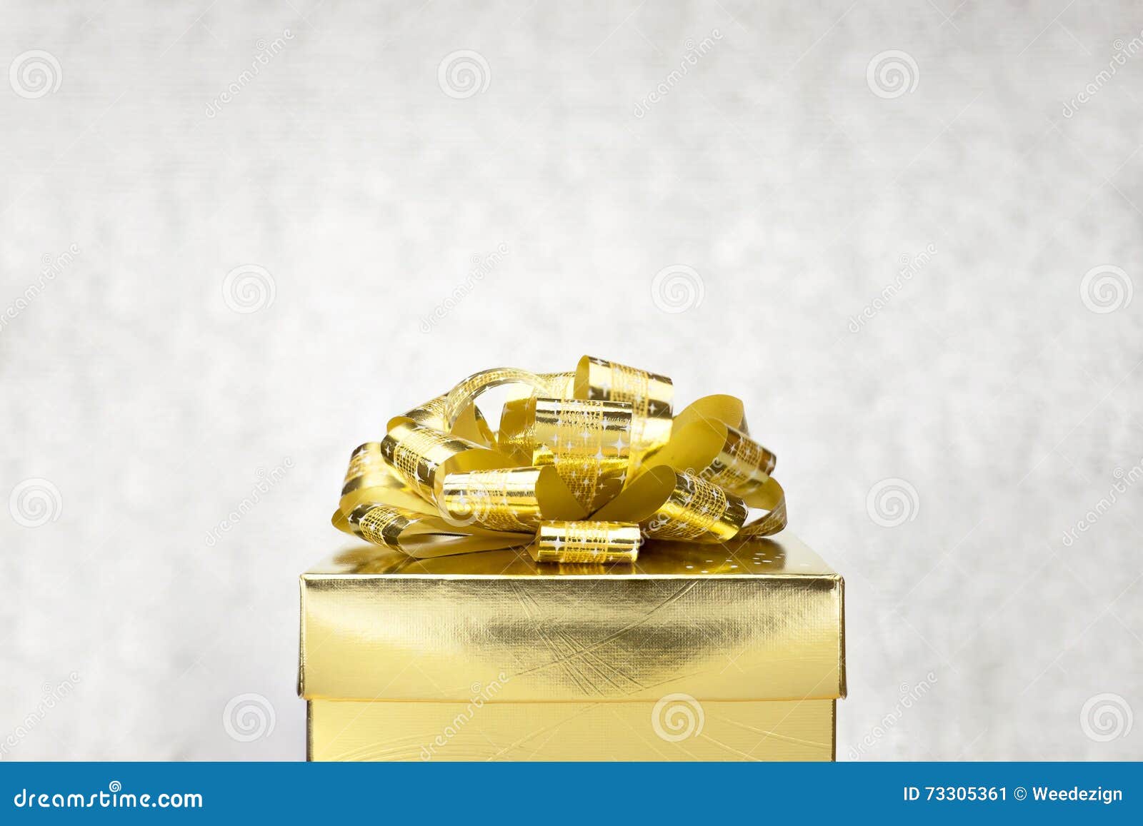 close up golden present box with big bow at bokeh white blur background, leave space on top to adding your content